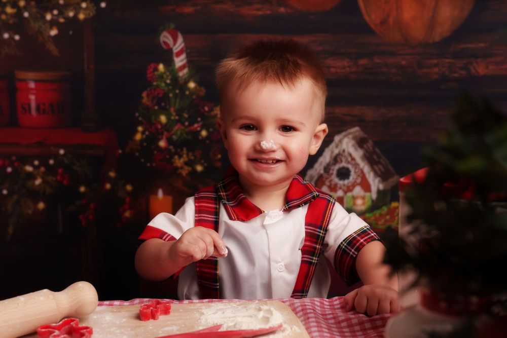 A child in red and white clothing sits at a table with holiday decorations and a small Christmas tree in the background.