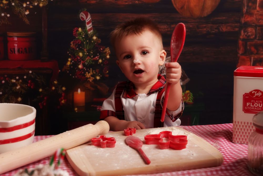 A cozy Christmas scene with a child making cookies on a red and white checkered tablecloth beside holiday decorations.