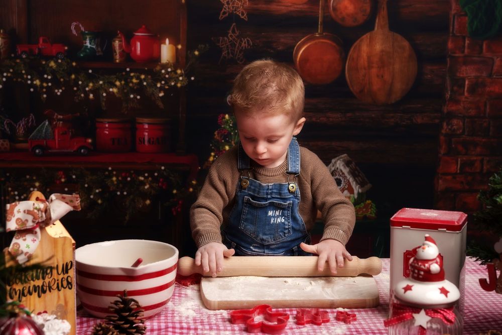 Child rolling out dough on a red and white checkered tablecloth with holiday decorations in the background.