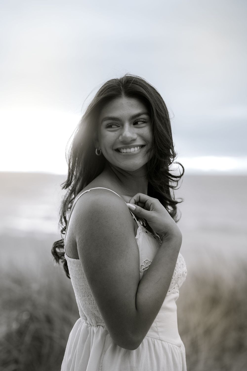 Black and white portrait of woman smiling joyfully against cloudy sky.