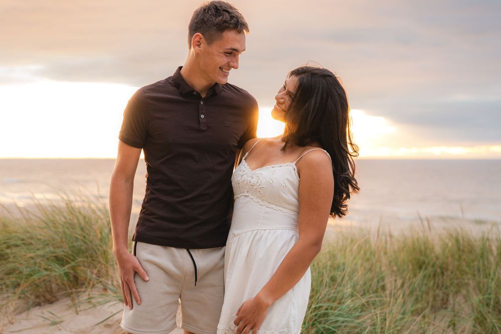 Couple walking together on beach path during sunset.