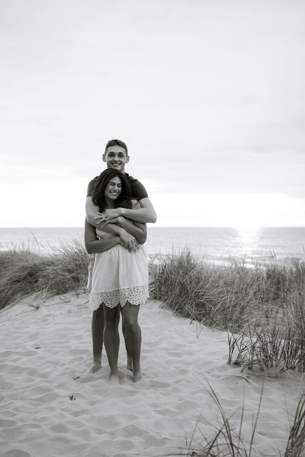 Black and white photos of couple sharing intimate moments on sandy beach.