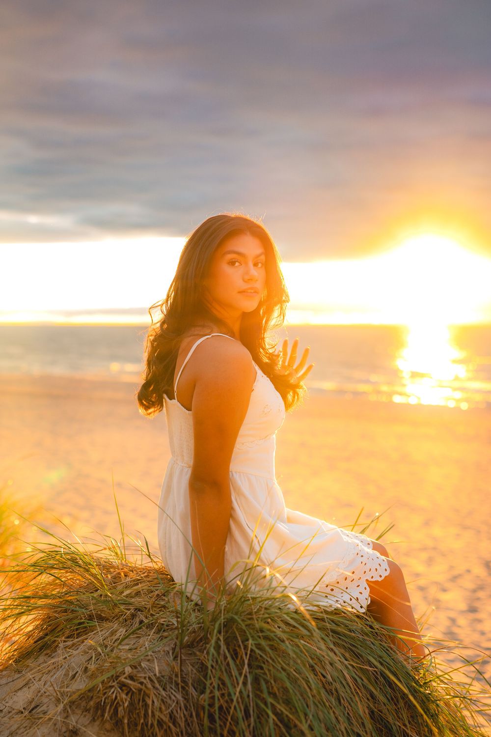 Woman relaxing on beach grass during dramatic sunset.