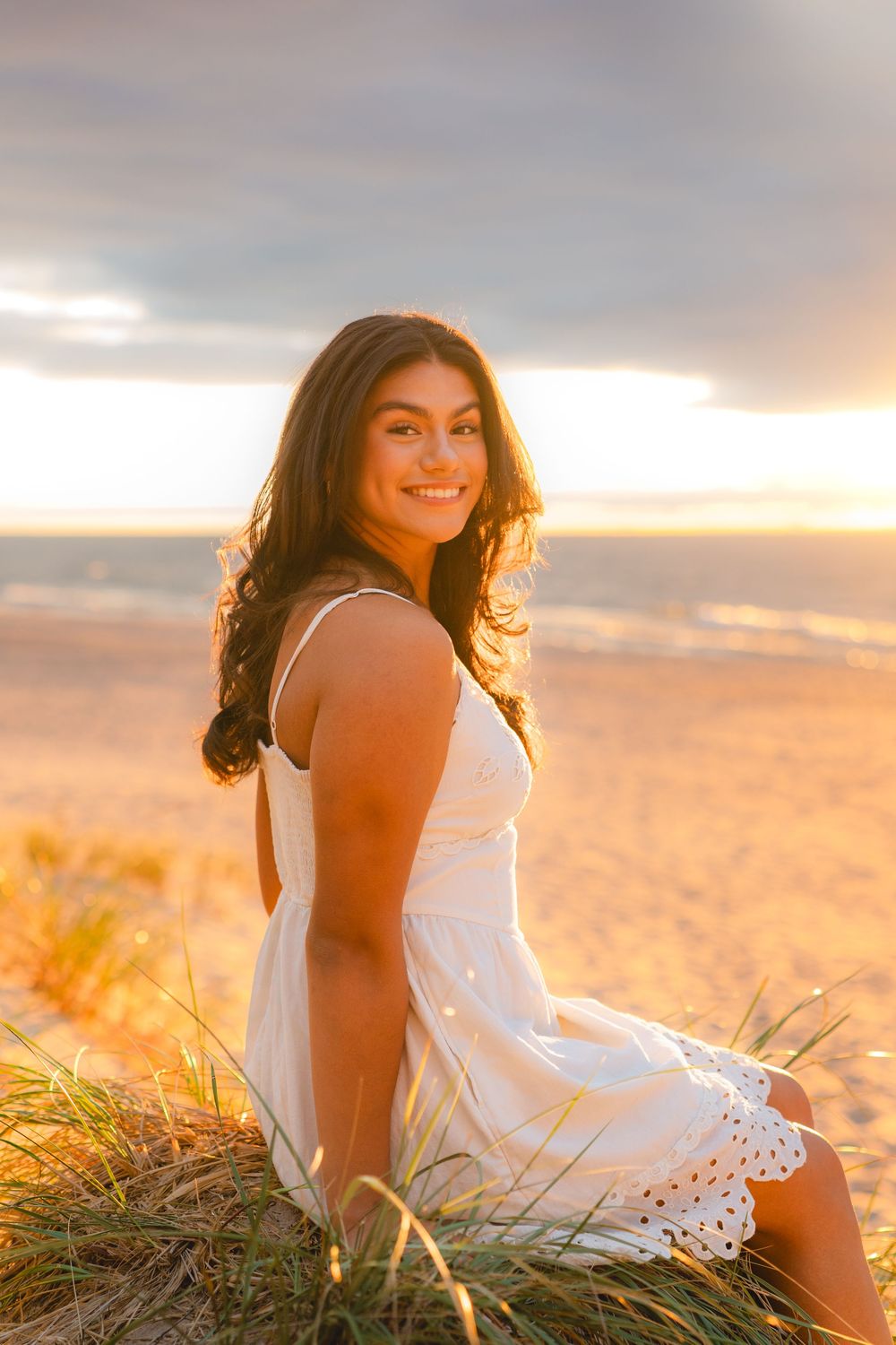 Woman in white sundress poses gracefully on beach during golden hour.