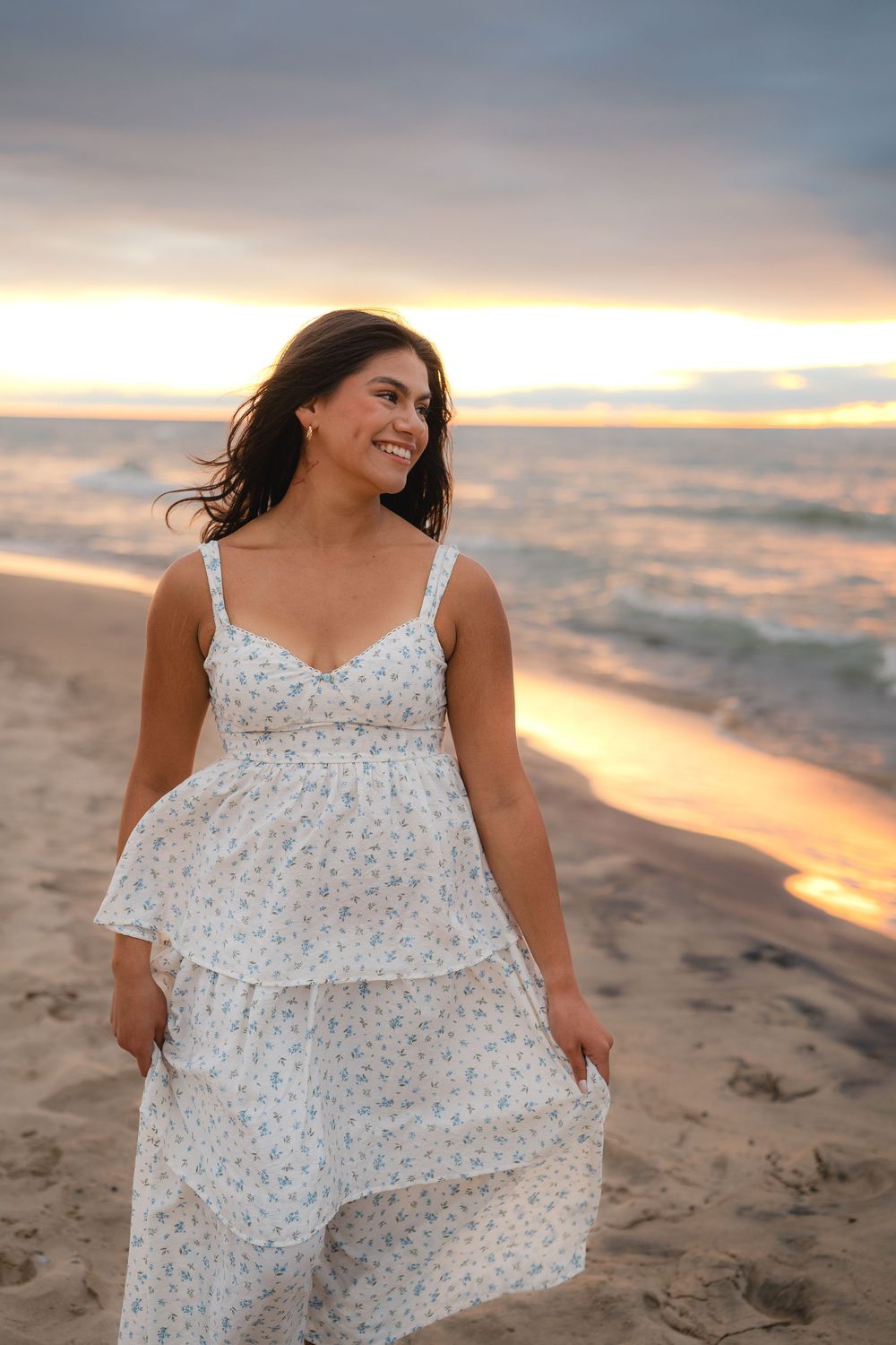 Woman in floral dress twirling playfully on beach at sunset.