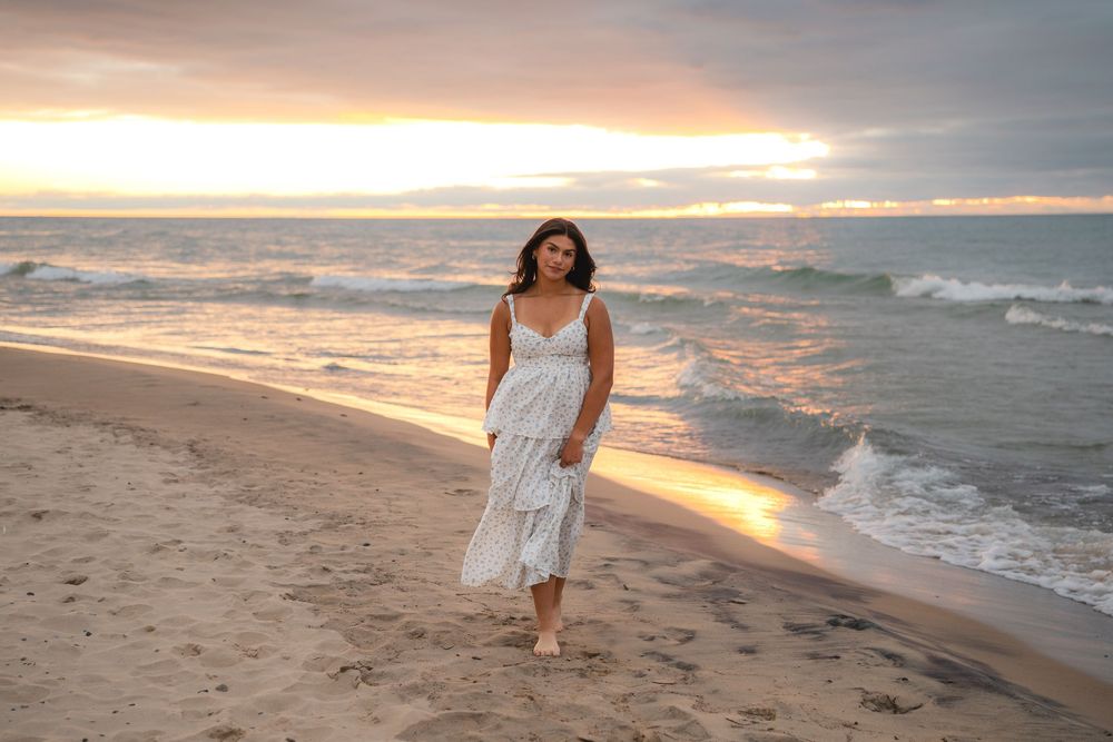 Woman walking along shoreline during dramatic beach sunset.