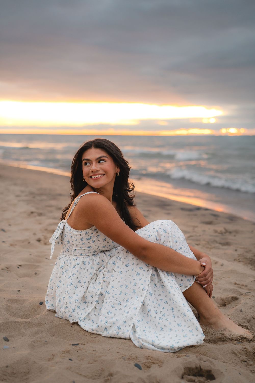 A person in a white floral dress reclines on sandy beach at golden hour.