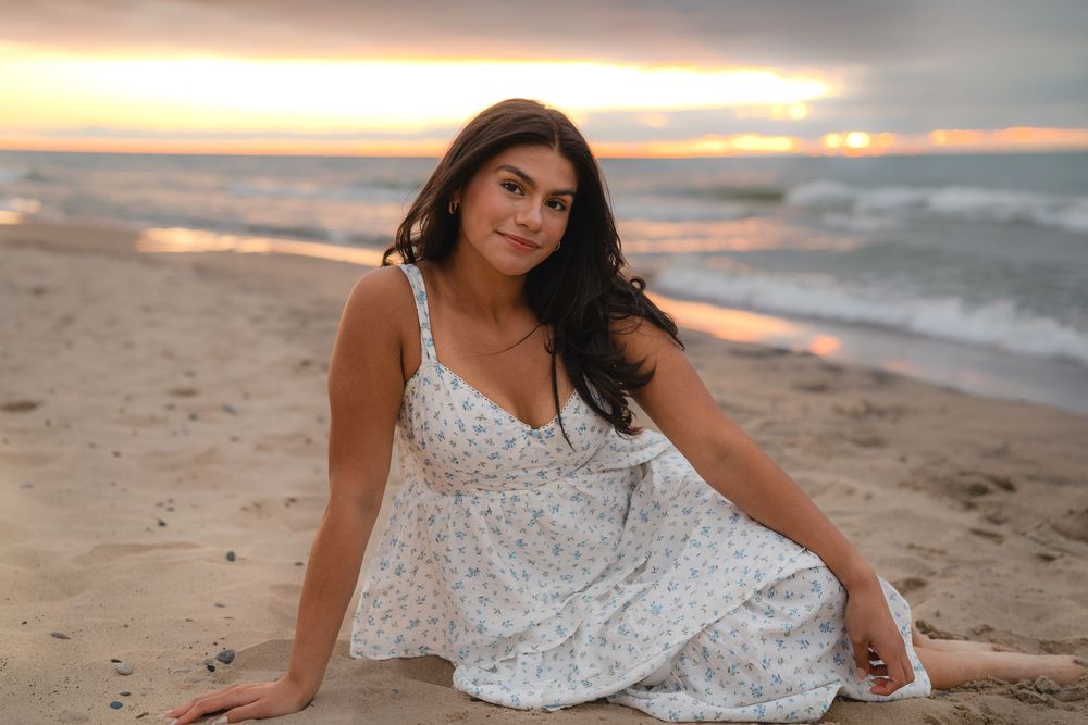 A person in a flowing white dress poses on the beach during a dramatic sunset.