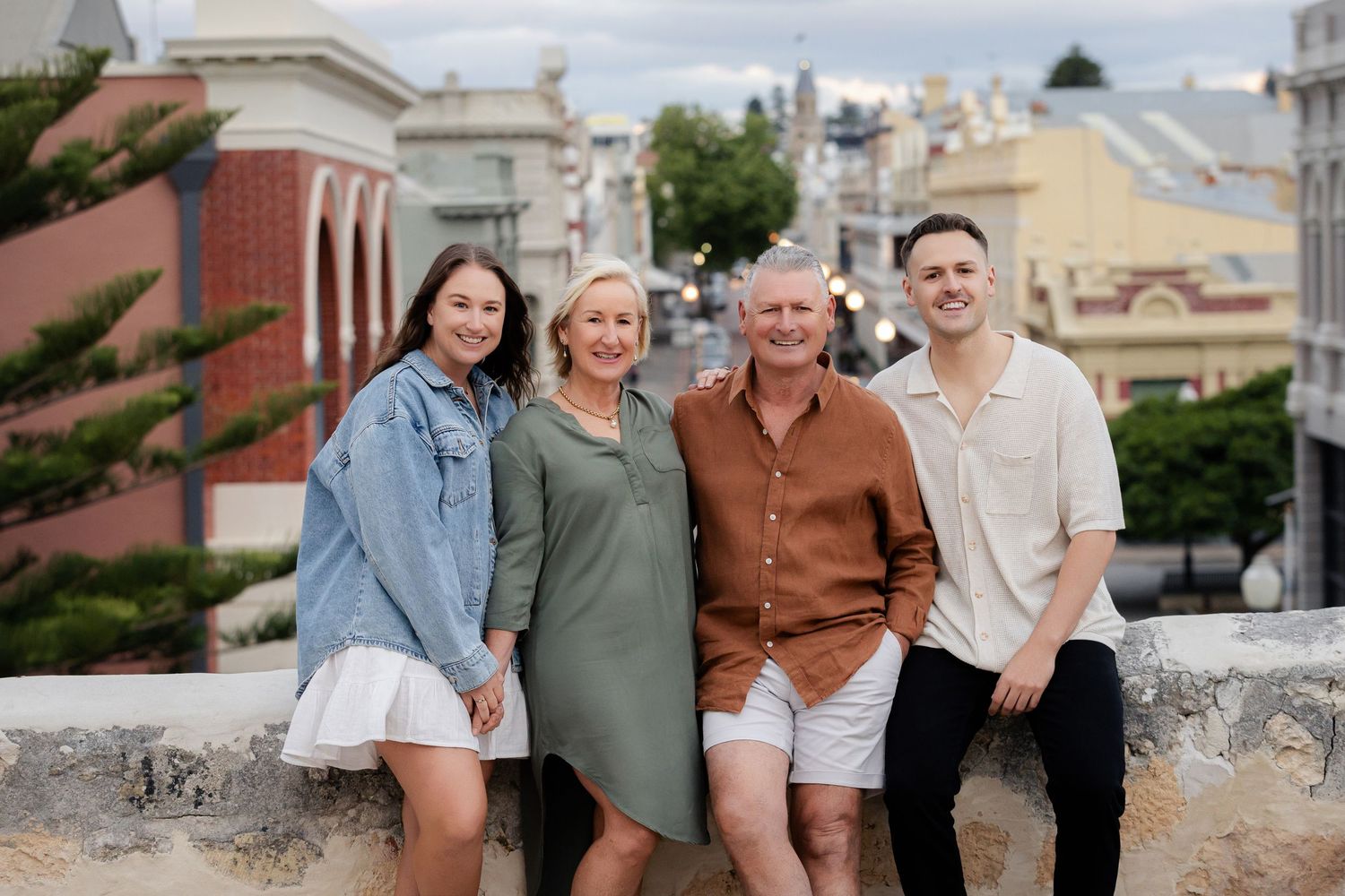 A group of people in coordinated casual outfits pose together outdoors against a light colored building.