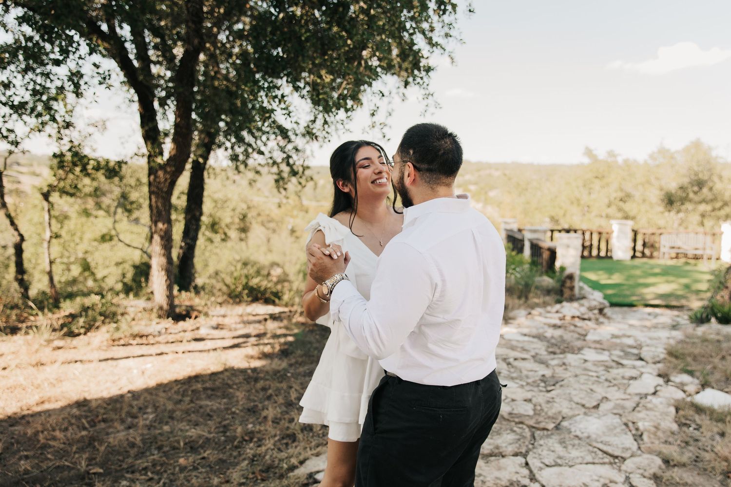 A couple in white clothing embraces on a stone pathway during a romantic outdoor photo session at sunset.