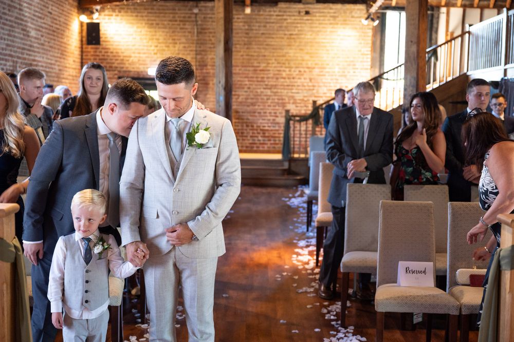 The groom and his young son are waiting nervously for the bride on the barn at Cooling Castle. Guests behind looking on.