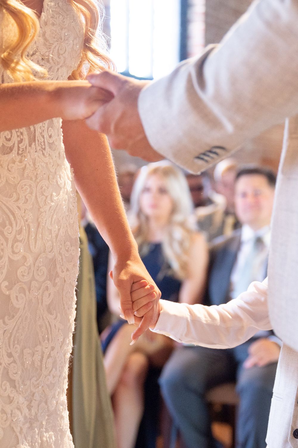 Close-up of the bride, groom, and their young son holding hands during their wedding ceremony at Cooling Castle Barn.