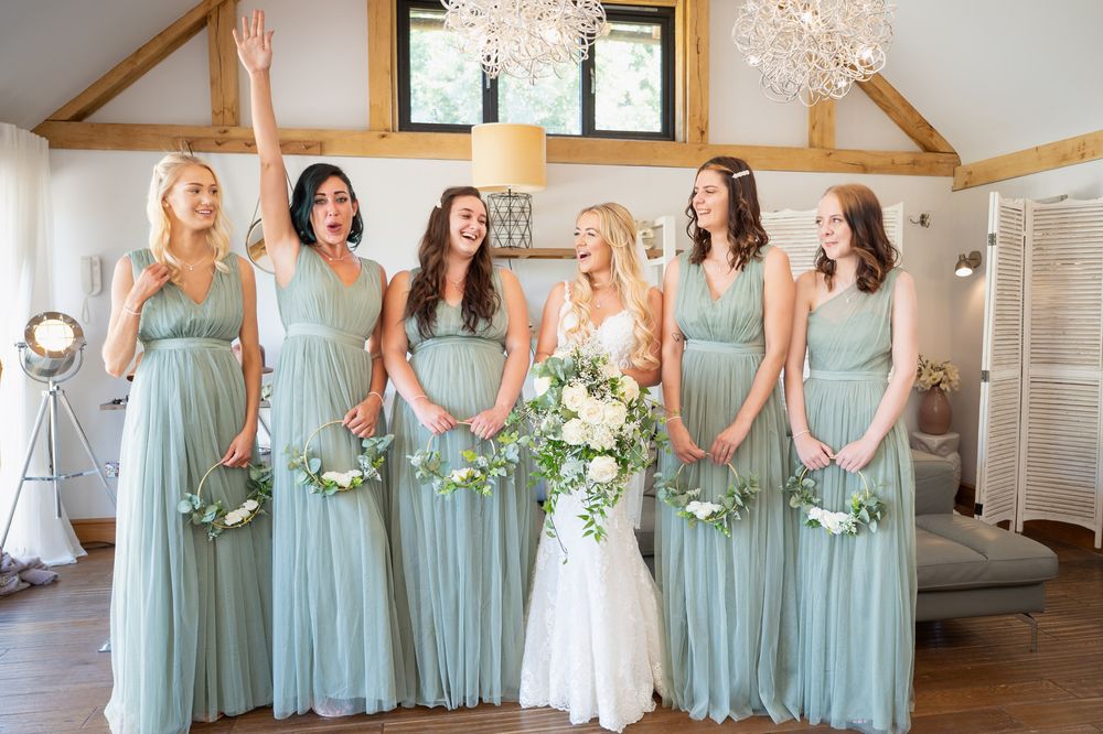 Bridal party wearing seafoam green bridesmaid dresses stand together holding white floral bouquets.