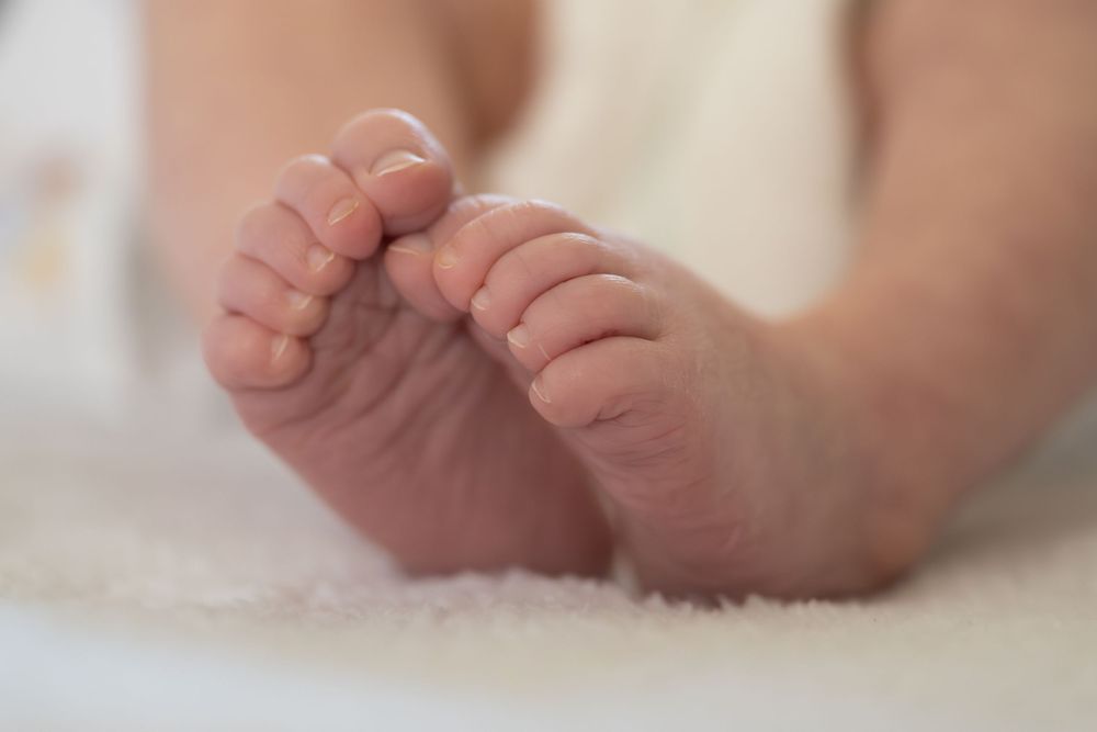Close-up view of tiny newborn baby feet with wrinkled skin against a soft white background.