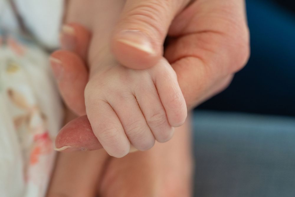 A tiny baby hand gently grasps an adult finger in a tender moment of connection.