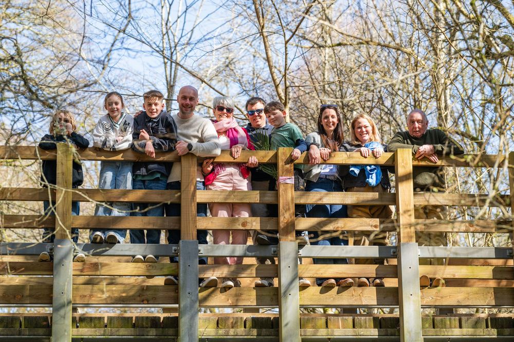 A group of people stand together smiling on a wooden observation deck surrounded by trees.