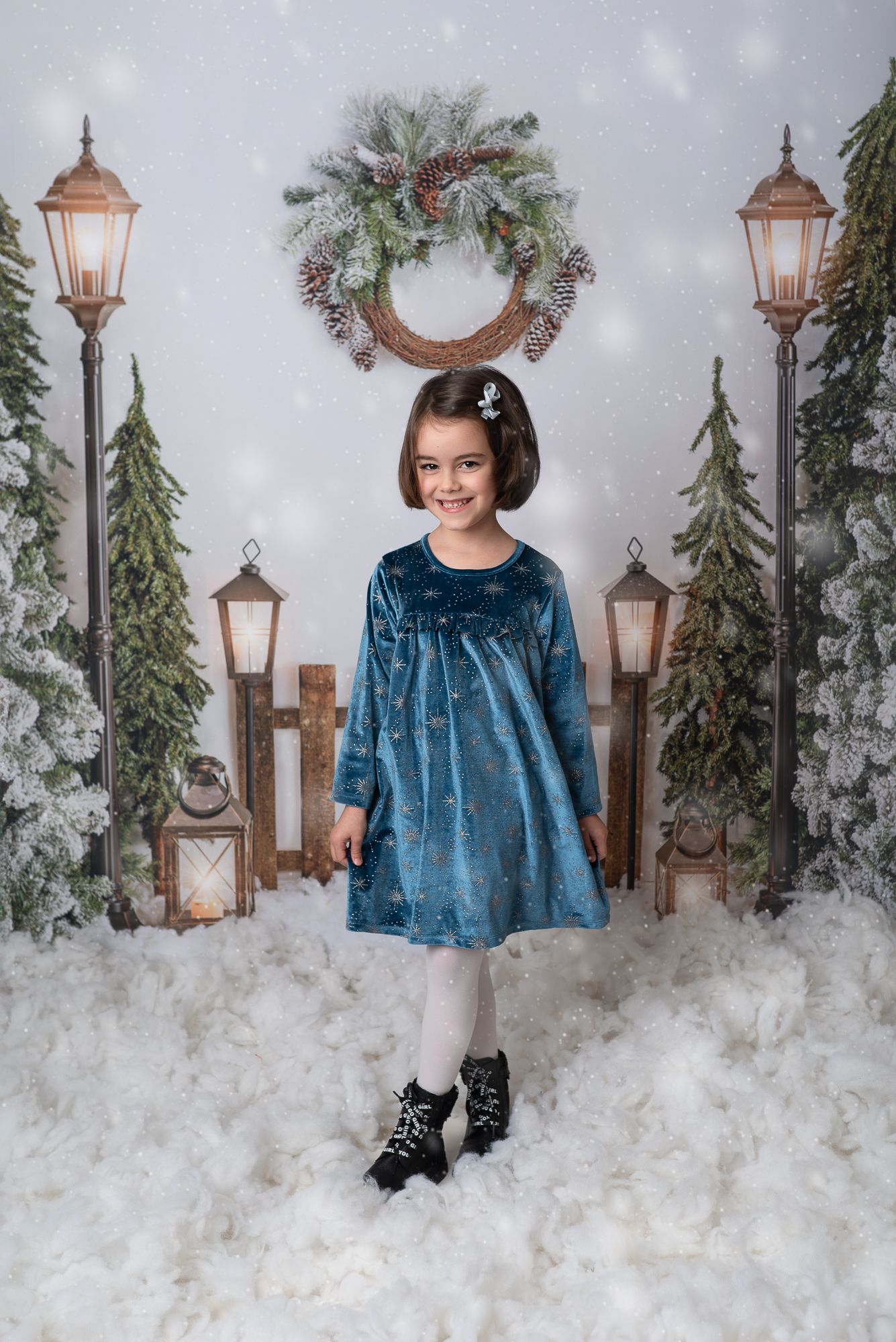 A winter photo session with decorative lamp posts, evergreen garlands, and artificial snow creating a magical holiday scene.