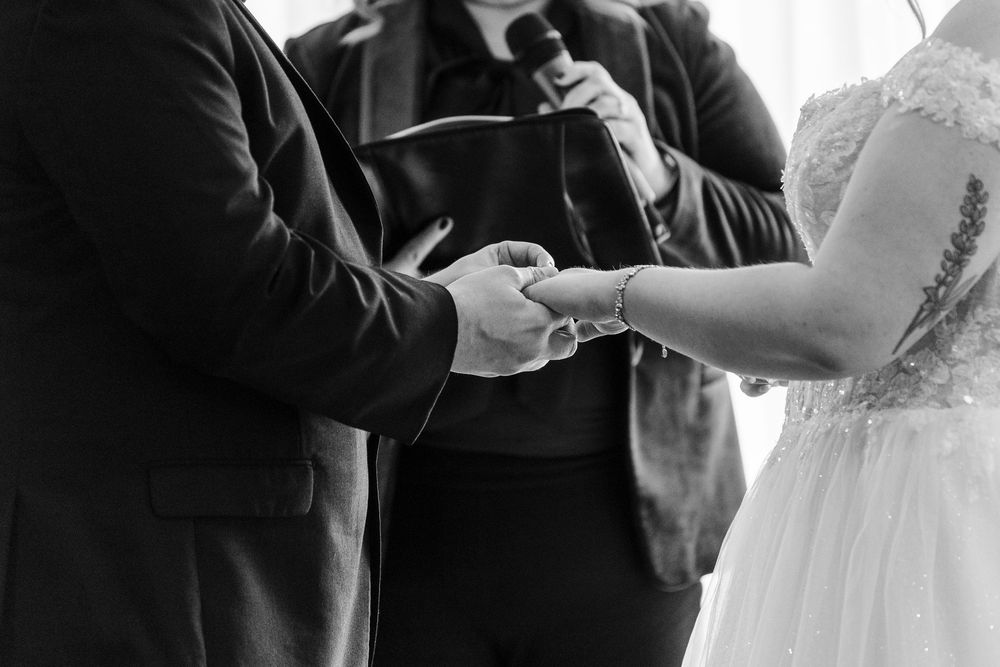 Black and white wedding ceremony photos showing close-up details of ring exchange and hands during vows.