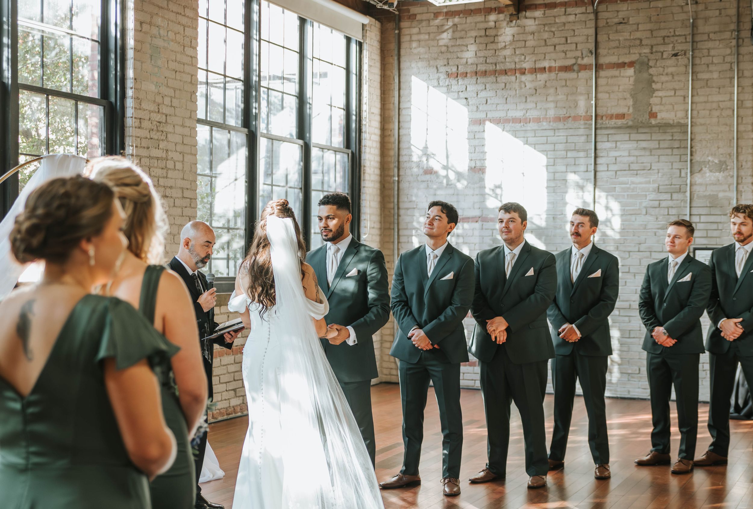 Wedding ceremony in industrial brick venue with wedding party lined up along exposed brick wall.
