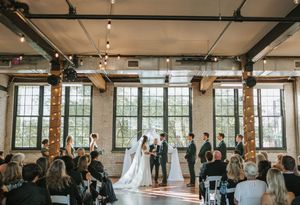 Wide angle view of wedding ceremony setup in rustic industrial space with natural lighting.