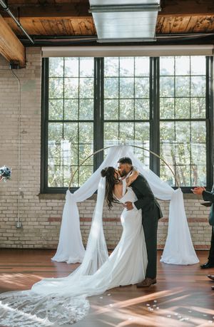 A romantic first look moment unfolds in a sunlit industrial wedding venue with exposed brick and wooden beams.