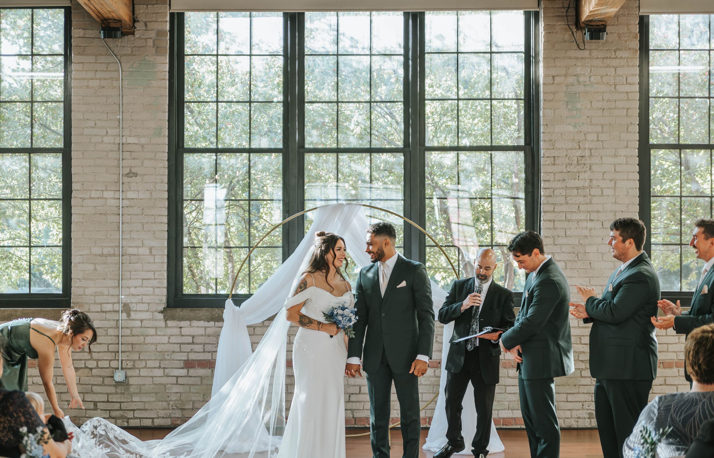 Panoramic wedding ceremony shot in bright loft space with large windows and exposed brick walls.