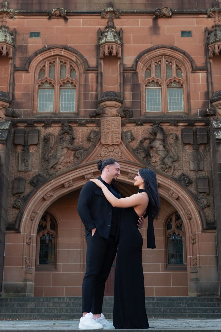 A couple embraces in front of an ornate gothic church facade with detailed stone carvings.
