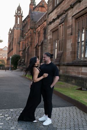 A couple shares a romantic moment in front of a gothic church building with cobblestone pavement.