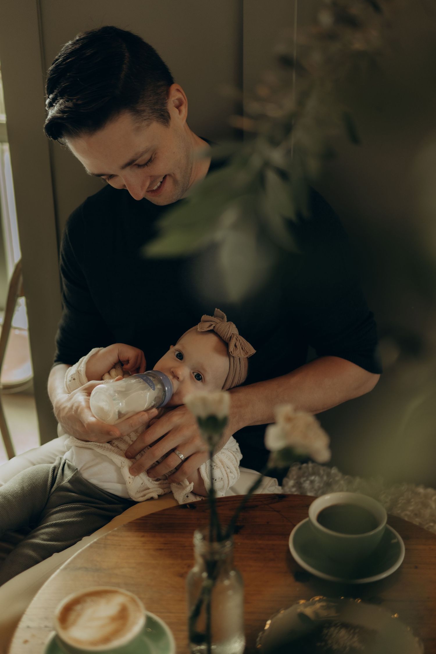 a man feeding his baby with a bottle in a café while being captured by vacation photographer in Stockholm
