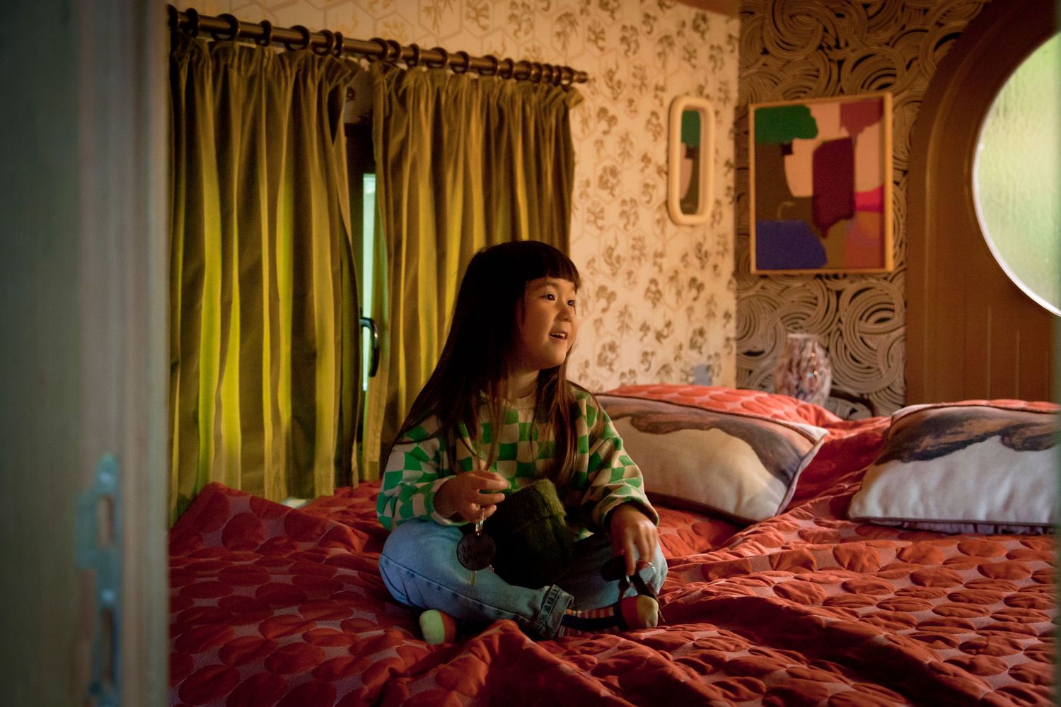 A dark interior scene shows a dimly lit bedroom with a red bedspread and floral wallpaper in vintage style.