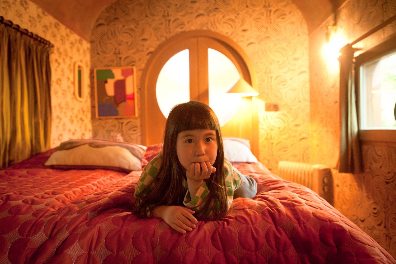 Cozy bedroom interior with warm lighting features ornate wallpaper and plush red bedding in vintage style decor.