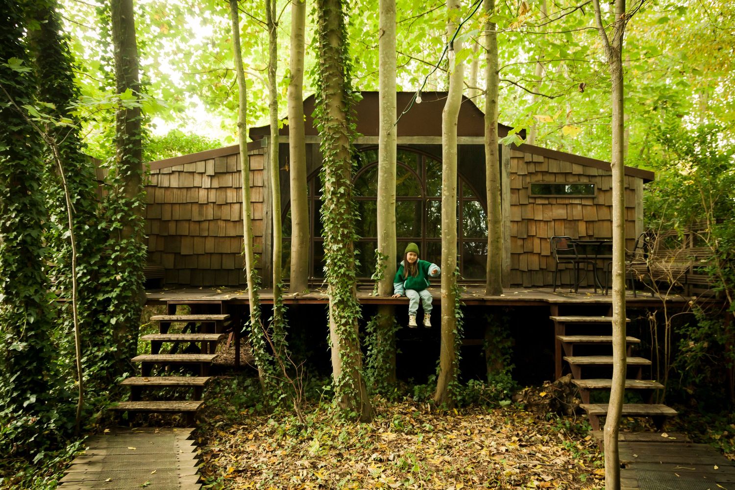 A series of wooden steps and platforms wind through a lush green forest setting with brick walls and natural foliage.