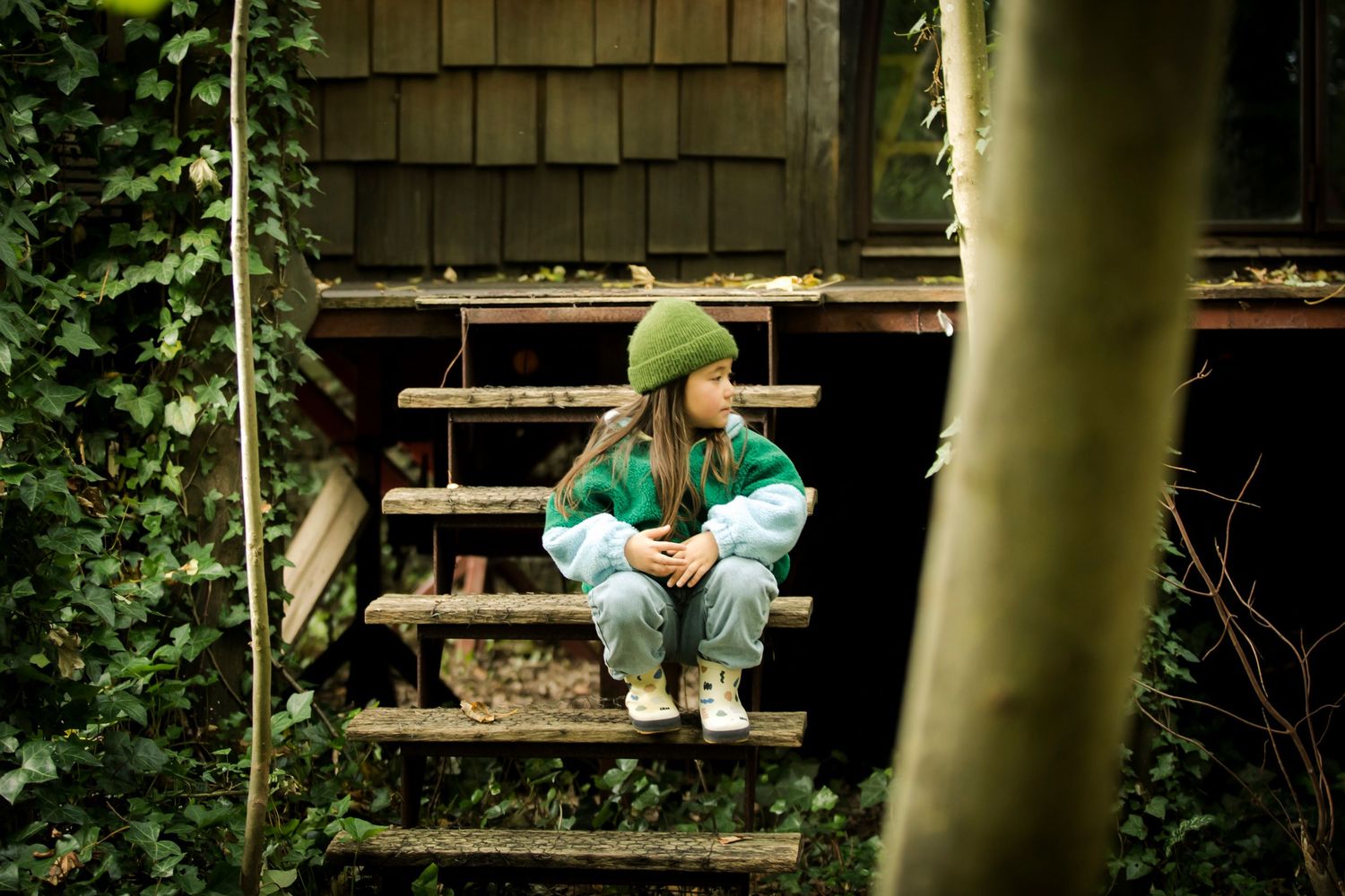 Someone sitting on a wooden deck in green pants while surrounded by lush forest vegetation.