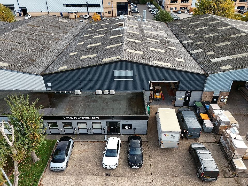 Aerial view of commercial warehouse buildings with white roofs and parking lots in an industrial area.