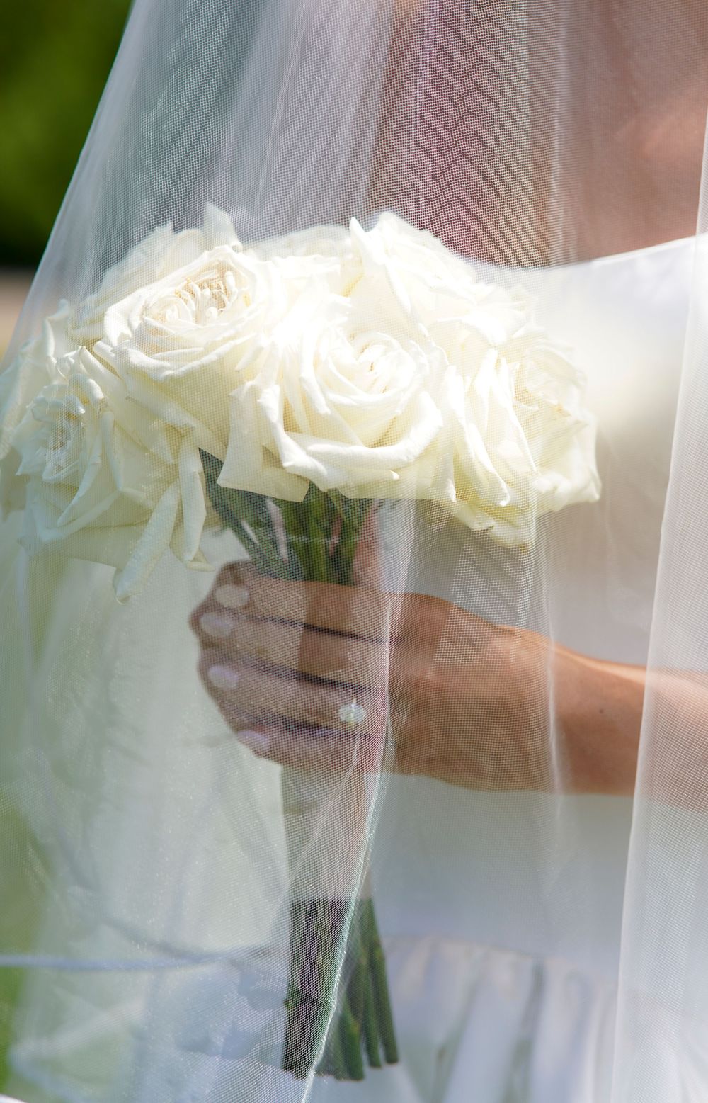 A delicate bridal bouquet of white roses wrapped in twine is held through a sheer veil.