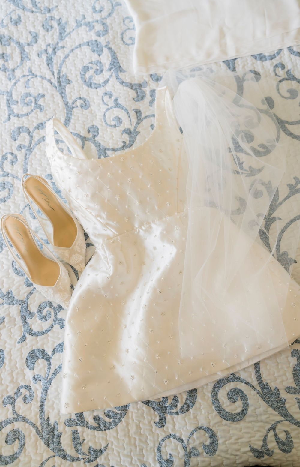Delicate white lace wedding dress fabric with intricate blue damask pattern in background.