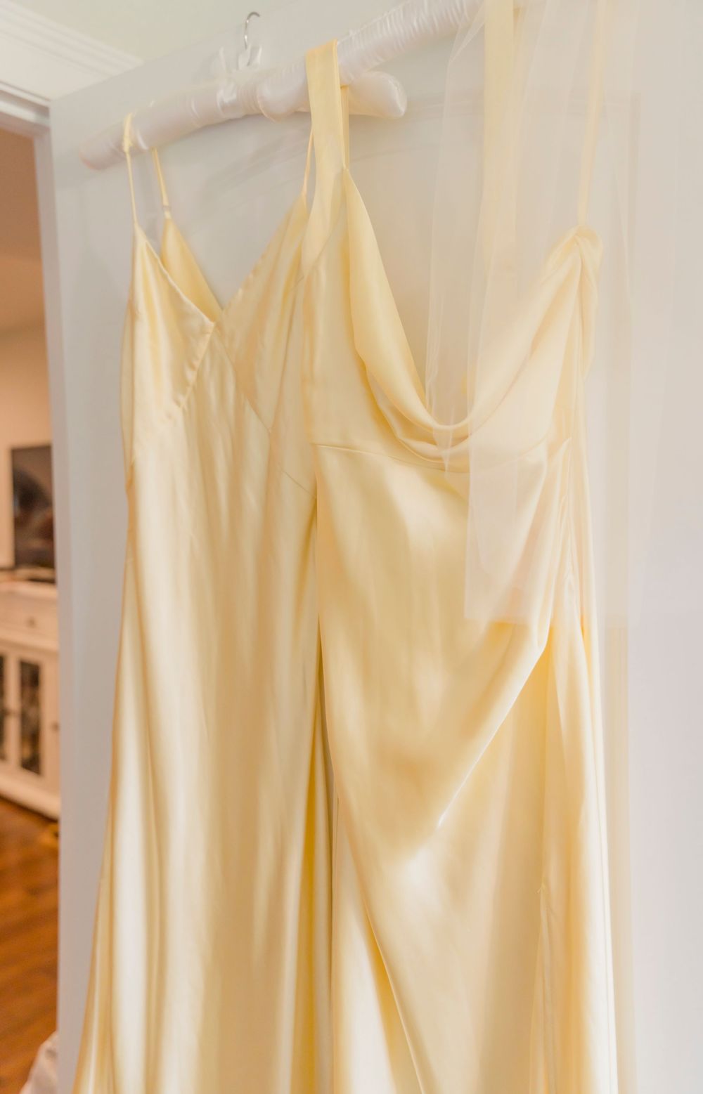 Row of pale yellow bridesmaid dresses hanging on white hangers against a white wall.