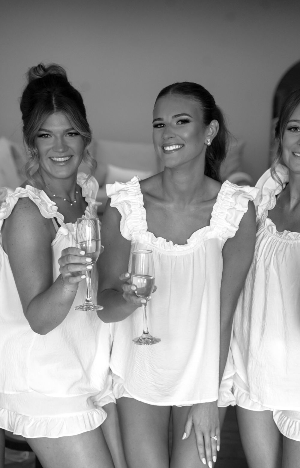 Group wearing matching white ruffled tops toasting with champagne glasses in black and white.