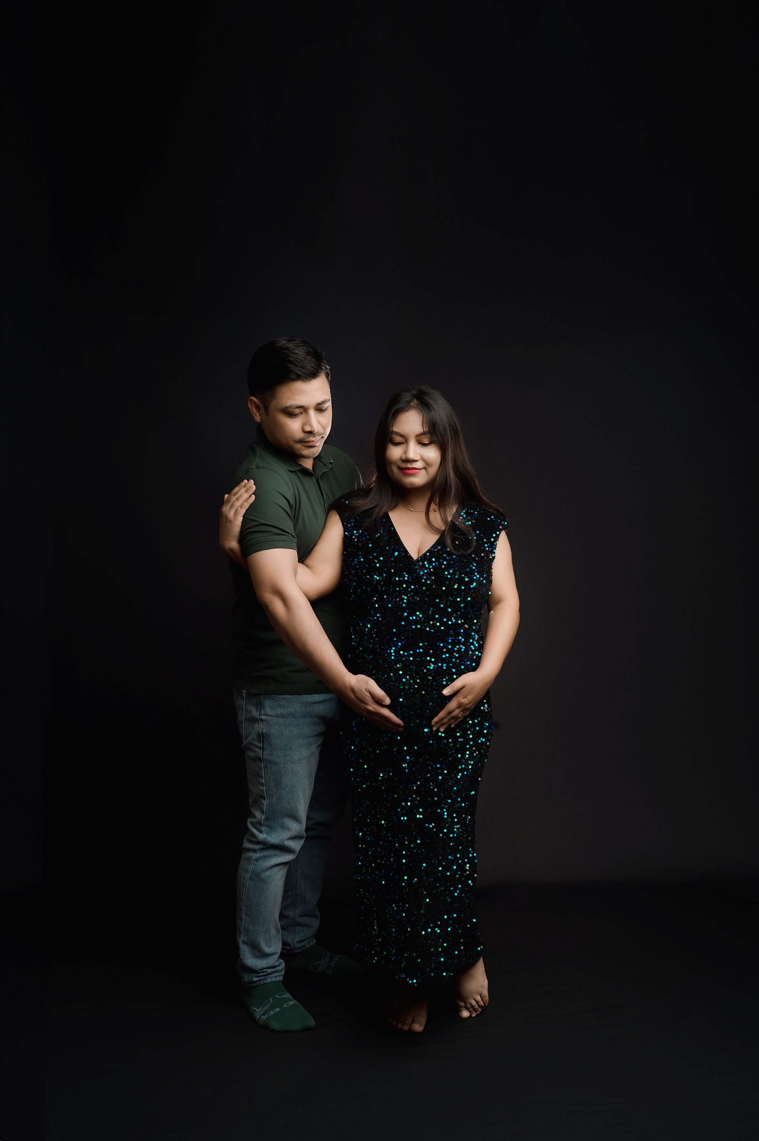 A couple in casual attire poses together against a dark background in a romantic photoshoot series.