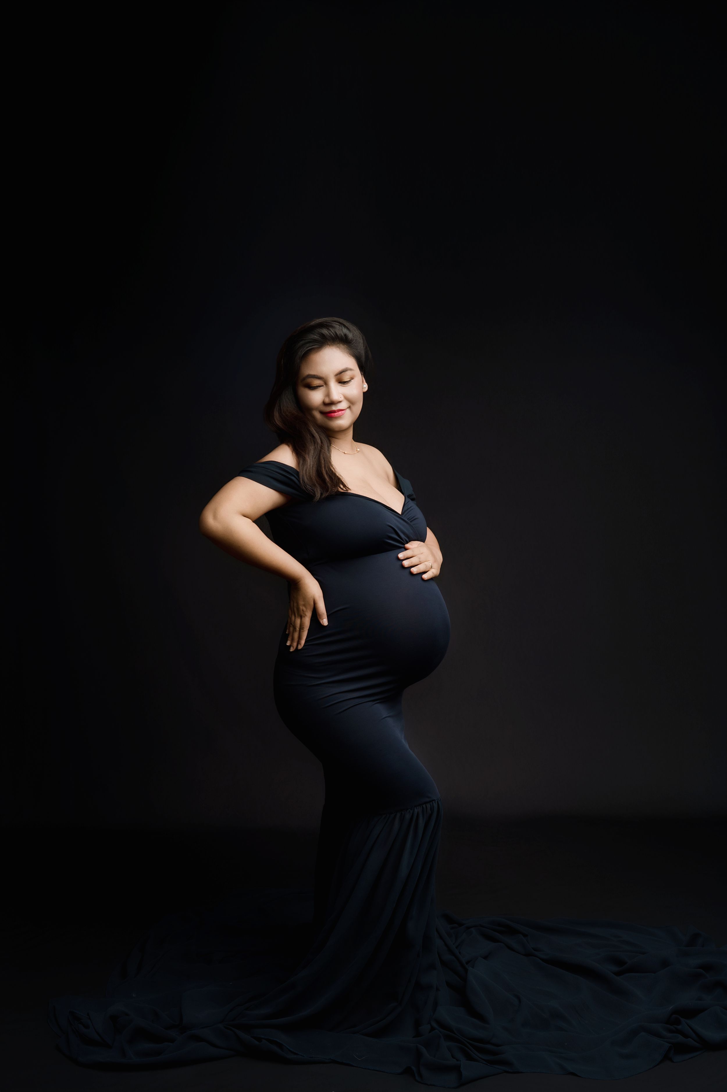 A woman in a flowing black dress performs an elegant dance pose against a dark background.