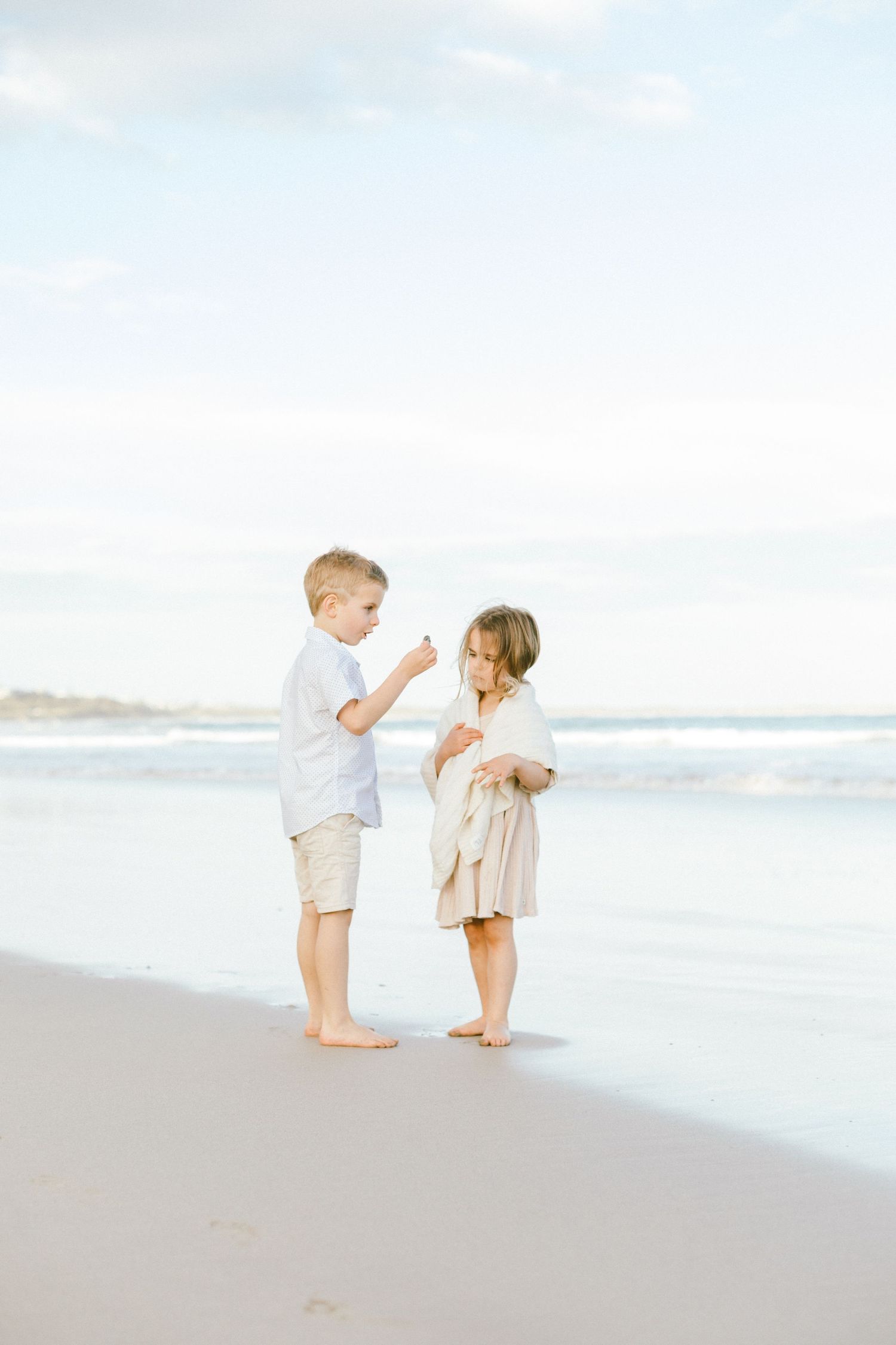Two small children in light colored clothing play together on a peaceful beach at sunset.