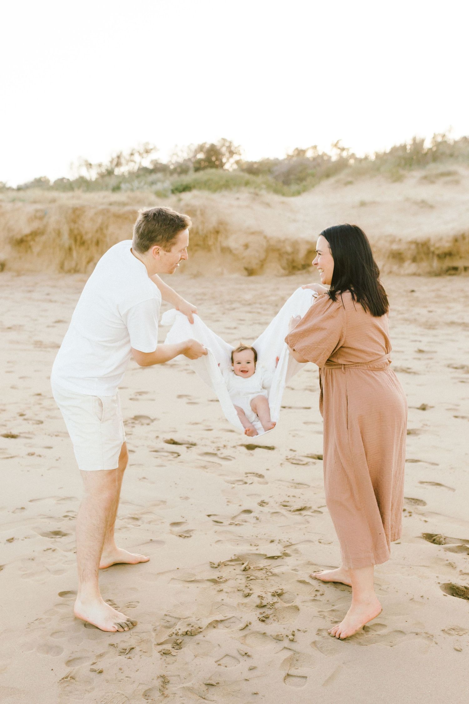A sequence of photos showing a family playing and swinging a small child on a sandy beach at sunset.