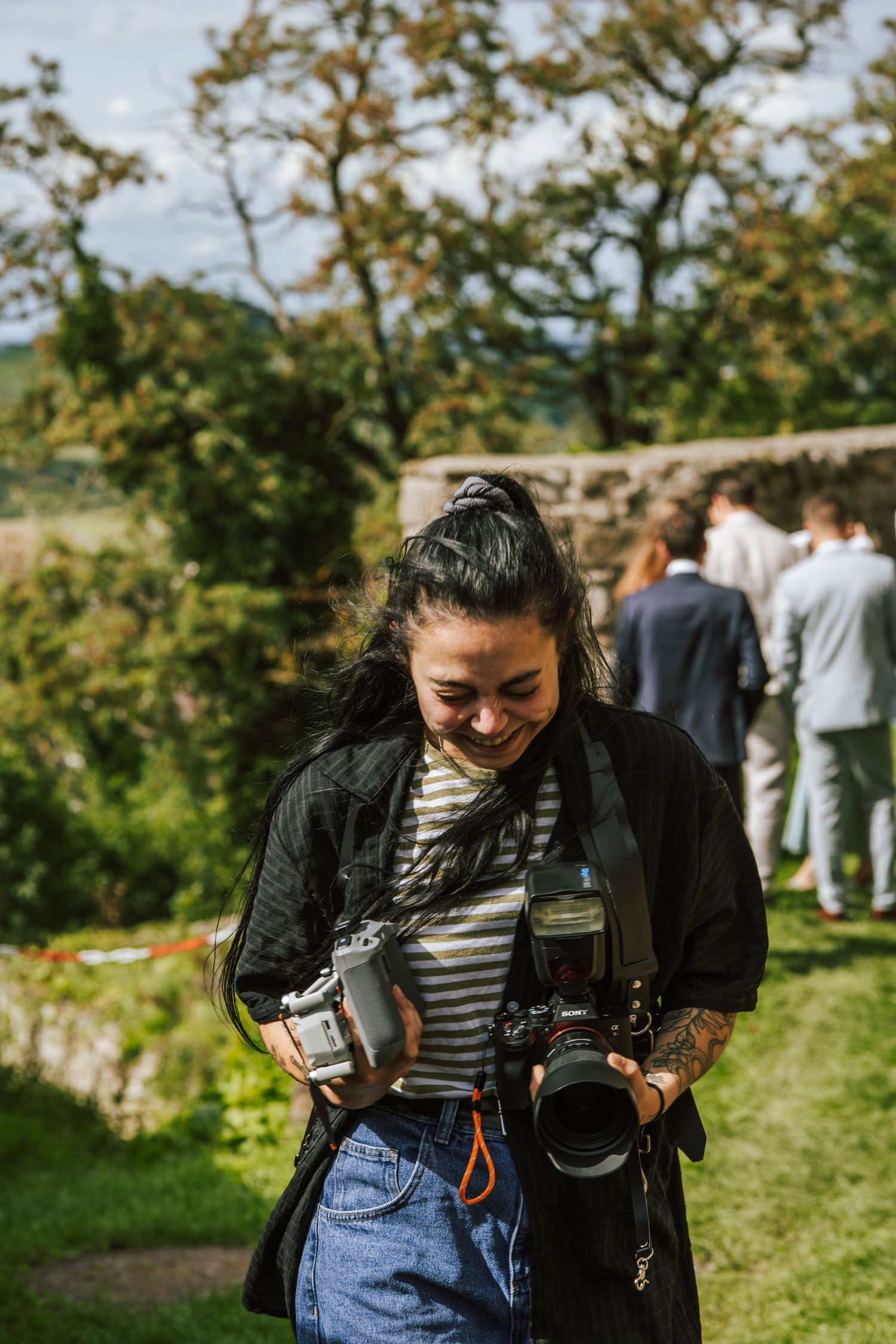 Photographer with multiple cameras laughing during outdoor event.