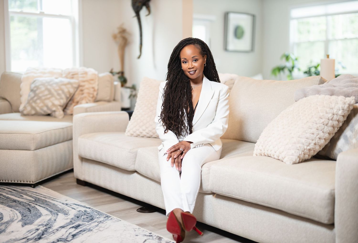 A woman relaxes on a plush beige sofa in a bright, modern living room with natural lighting.