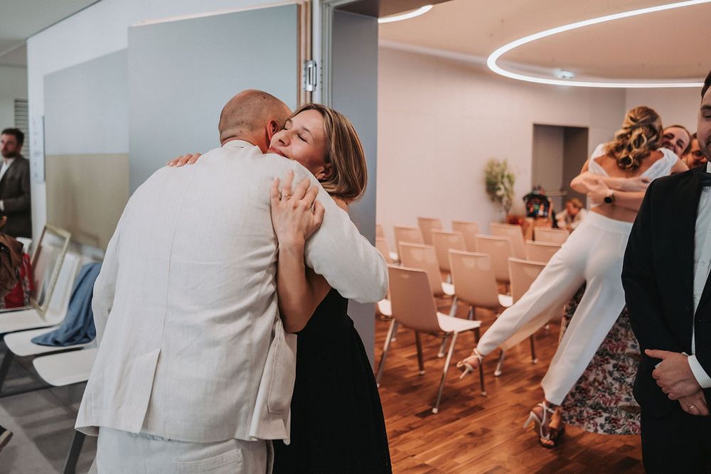 Guests hugging and showing affection during a wedding reception in a modern venue with circular lighting.