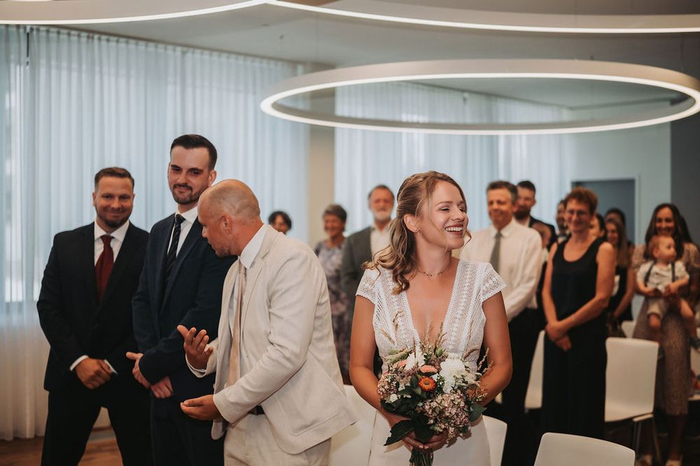 Wedding attendees gather in a modern event space with circular ceiling lights and white curtains.