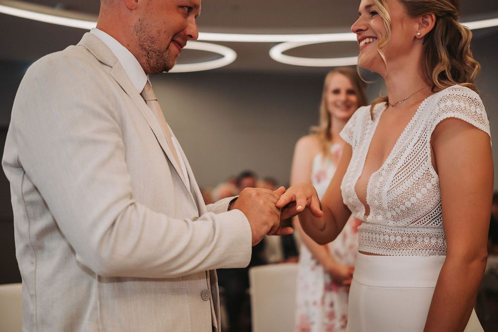 A couple exchanges rings during an intimate indoor wedding ceremony with circular lighting overhead.