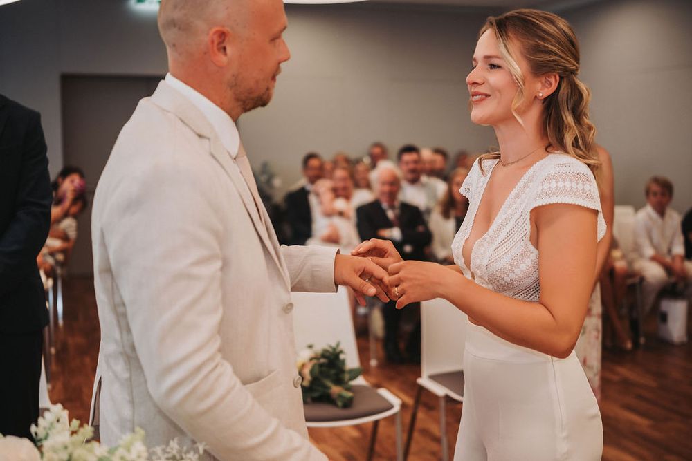 A couple holds hands during an intimate wedding ceremony in a modern indoor venue with wooden floors.
