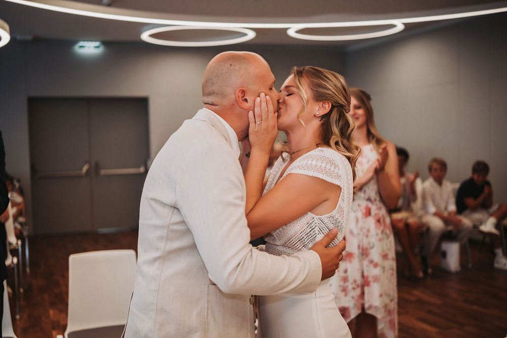 A couple shares their first kiss as newlyweds during a wedding ceremony in a modern indoor venue.