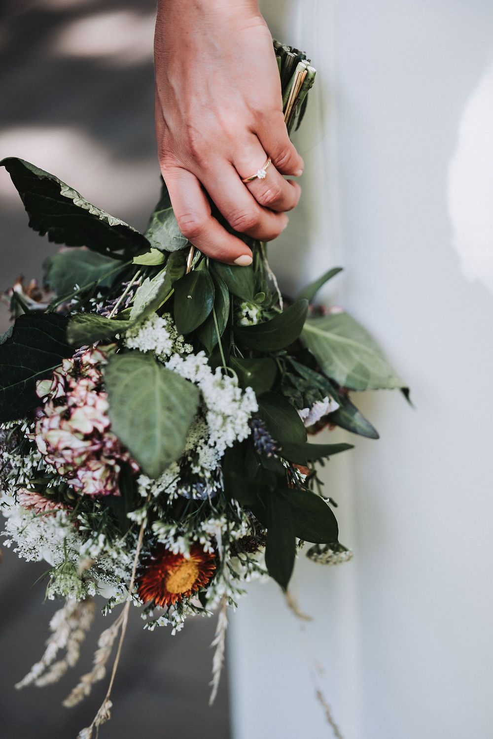 Hands arranging delicate white and pink flowers in a rustic floral arrangement with greenery.